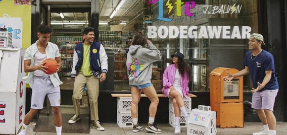 Five people hang out in front of a bodega. One is sitting on a crate. Another holds a basketball.